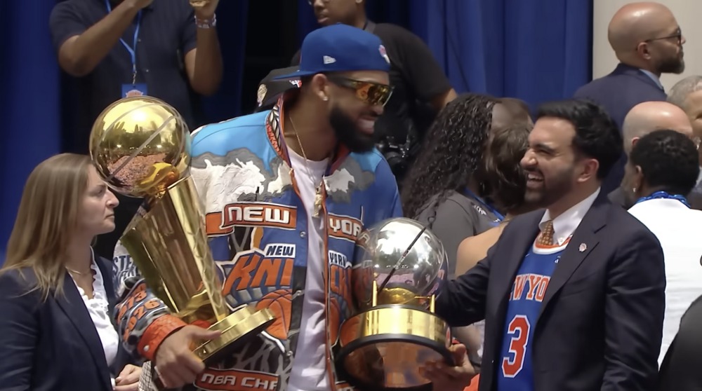 Knicks player greeting a city official while holding the championship and Eastern Conference trophies