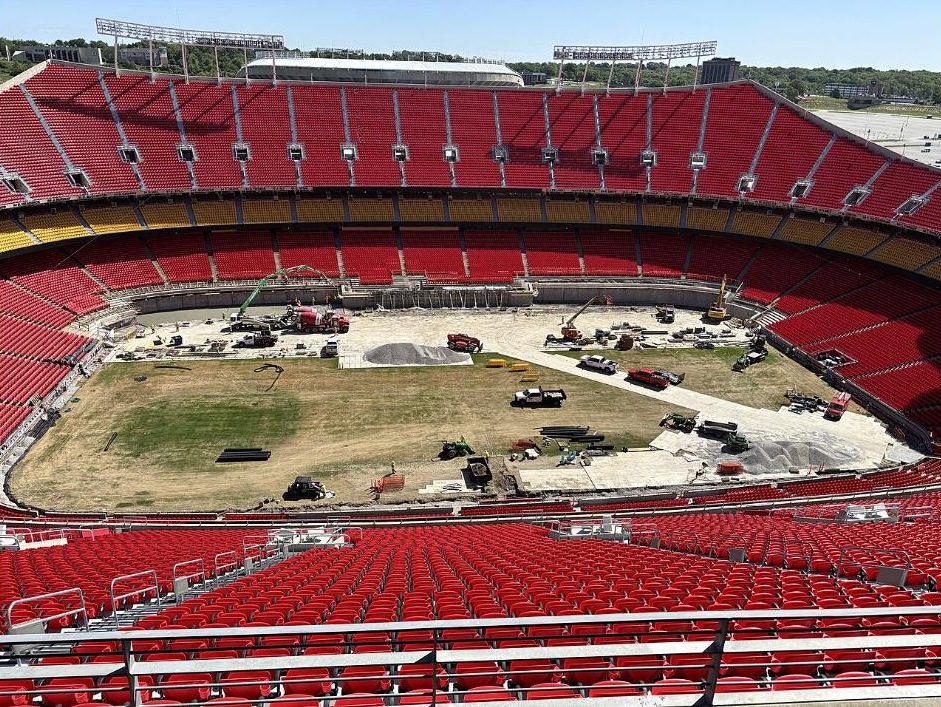 Arrowhead Stadium during World Cup preparations, with heavy equipment on a field stripped of turf and ringed by red seats