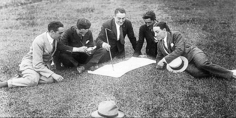 Black-and-white photo of Hándicap and colleagues unrolling plans on the grass of the Balaídos site, circa 1928, before the ground was built