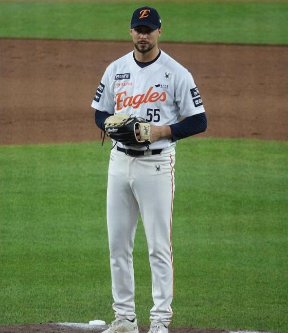 A pitcher in a white Eagles home uniform with sponsor patches on the chest and sleeves, standing on the mound holding a glove