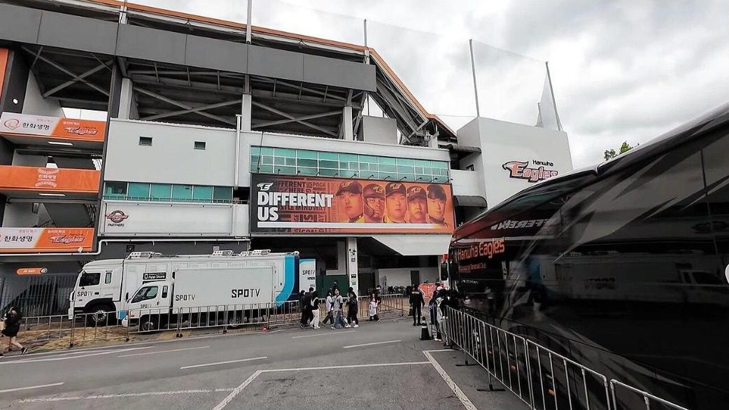The Hanwha Life and Eagles signs on the outer wall of the old Daejeon Hanbat Baseball Stadium, with people and a broadcast truck in front