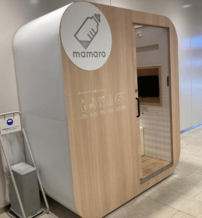 나무 질감의 패널에 ‘mamaro’ 로고와 젖병 그림이 붙은 1인용 수유실 부스, 옆에 서 있는 우산 비닐 거치대