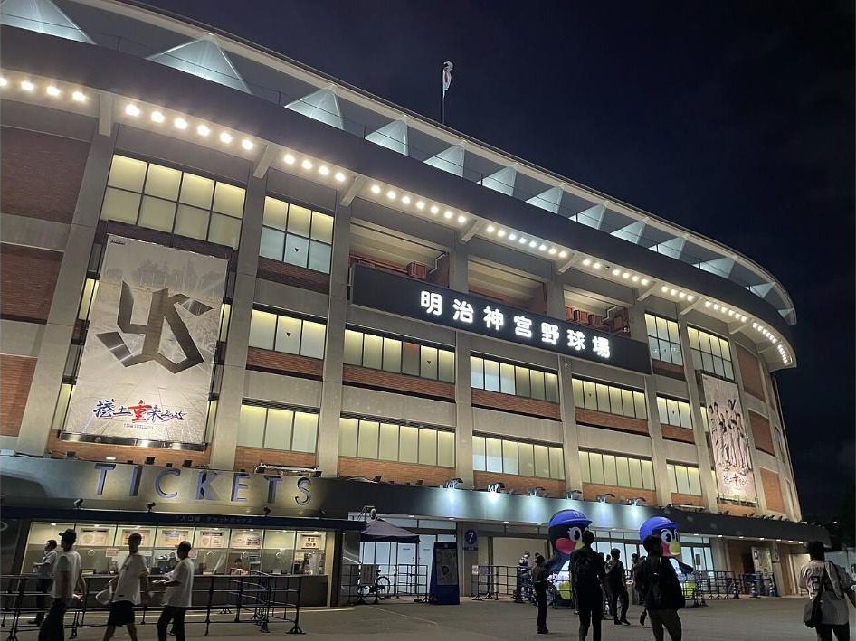 Meiji Jingu Stadium lit up at night with the ticket windows and mascot figures of Tsubakuro in front of Gate 7
