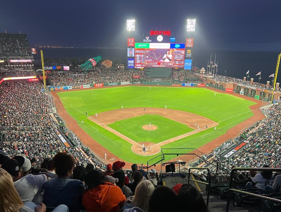 Oracle Park during a night game, with the stands, the center-field scoreboard and the bay beyond the outfield