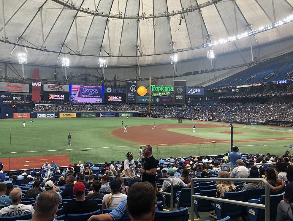 Inside Tropicana Field under the fixed dome roof during a baseball game, with outfield advertising boards and the stands visible
