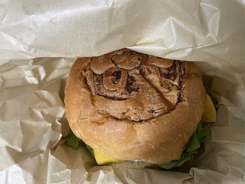 A wagyu burger wrapped in paper with the face of the mascot branded into the top of the bun
